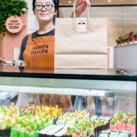 Sushi Sushi franchise employee places take out bag on sushi counter